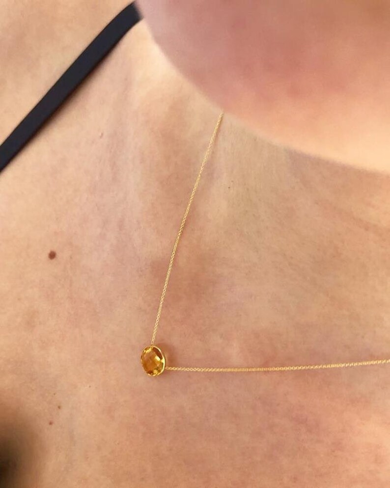May include: A gold chain necklace with a single, round, yellow gemstone pendant.