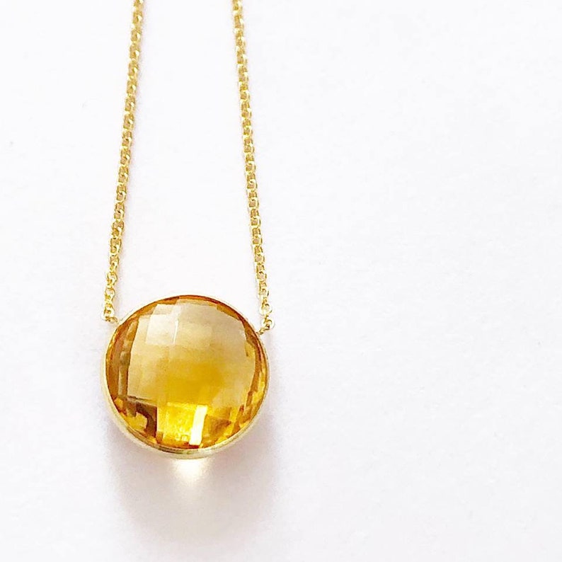 May include: A gold chain necklace with a large, round, faceted, yellow citrine gemstone pendant.