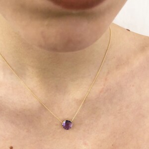 May include: A delicate gold chain necklace with a single, round, purple amethyst gemstone pendant.