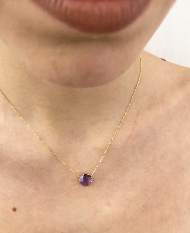 May include: A delicate gold chain necklace with a single, round, purple amethyst gemstone pendant.