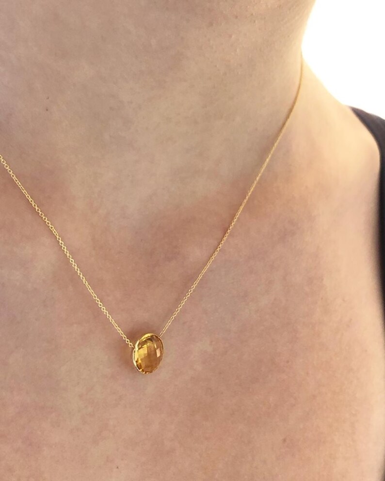 May include: A gold chain necklace with a single, round, yellow gemstone pendant.