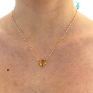 May include: A gold chain necklace with a round, faceted, yellow gemstone pendant.