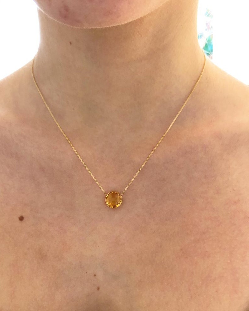 May include: A gold chain necklace with a round, faceted, yellow gemstone pendant.