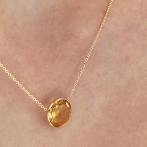 May include: A gold chain necklace with a round, yellow gemstone pendant.