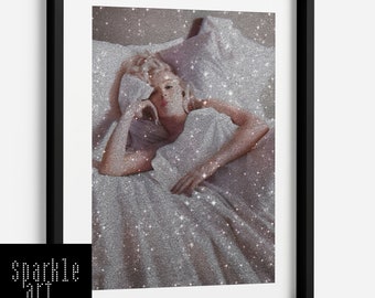 May include: A black and white photo of a woman lying in bed with a silver glitter overlay. The woman is wearing a white shirt and has her hair pulled back. The photo is framed in a black frame.