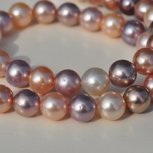 May include: A strand of pearls in shades of pink, purple, and white. The pearls are round and have a smooth, lustrous finish.