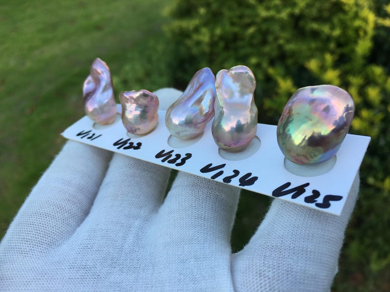 May include: Five iridescent baroque pearls of varying shapes and sizes are displayed on a white card. The pearls have a mix of pink, purple, and green hues. Each pearl is labeled with a black number.