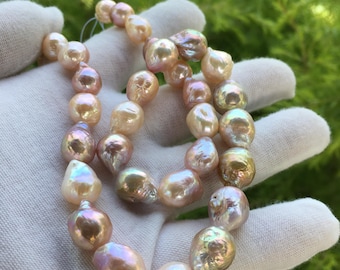 May include: A strand of iridescent, baroque pearls in shades of pink, peach, and cream. The pearls have irregular shapes and a lustrous finish, strung together to form a necklace. The background is a blurred green.