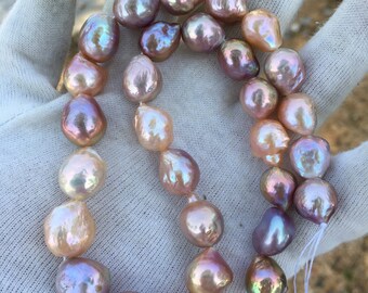 May include: A strand of iridescent baroque pearls in shades of pink, lavender, and white. The pearls are strung on a white thread and are displayed on a white surface.