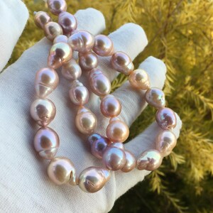 Può includere: Una collana di perle barocche rosa iridescenti. Le perle sono infilate su un filo trasparente e sono di dimensioni e forme diverse.