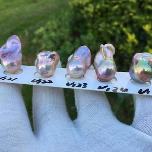 May include: Five iridescent baroque pearls displayed on a white card, each with a unique shape and color. The pearls range in hues from pink and lavender to green and gold. The card has black handwritten numbers.