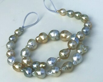 May include: A strand of baroque pearls in shades of gold, silver, and blue. The pearls are strung on a clear elastic cord with a knotted closure.