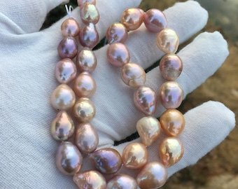 May include: A strand of iridescent pink and white baroque pearls. The pearls are strung on a white thread and are of varying sizes and shapes.