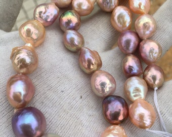 May include: A strand of baroque pearls with a variety of iridescent colors, including pink, peach, and lavender. The pearls are strung on a white thread and are displayed on a white surface.