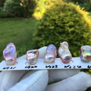 May include: Five iridescent baroque pearls of varying shapes and sizes are displayed on a white card. The pearls exhibit colors of pink, purple, and gold, with a shimmering, textured surface. Each pearl is labeled with a number.