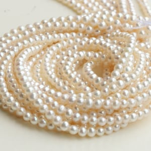 May include: A strand of white freshwater pearls, arranged in a circular pattern. The pearls are smooth and lustrous, with a slightly off-white color.