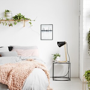 Pu&ograve; includere: Una camera da letto bianca con un letto, un comodino e una lampada. Il letto ha un piumone bianco e una coperta rosa. Il comodino &egrave; nero e ha una lampada dorata sopra. C'&egrave; una stampa incorniciata in bianco e nero sul muro sopra il comodino.