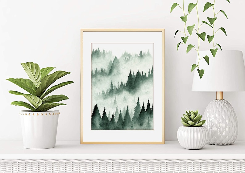 May include: A framed watercolor painting of a misty forest scene with green trees and a gold frame. The painting is on a white shelf with a potted plant and a lamp on either side.