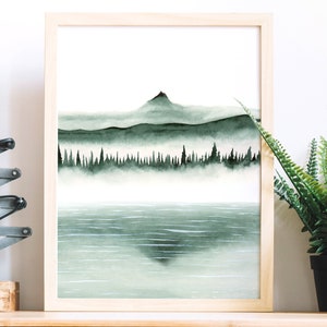 K&ouml;nnte beinhalten: Ein gerahmtes Aquarellbild einer Bergkette mit einem See im Vordergrund. Die Berge sind dunkelgr&uuml;n und von Nebel bedeckt. Der See ist hellblau und spiegelt die Berge wider.