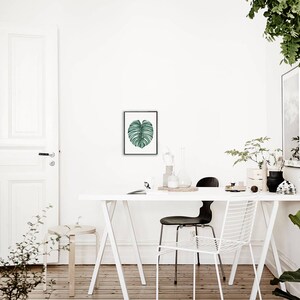 May include: A white table with a white chair and a black chair. There is a green leaf print on the wall and a plant in a pot on the table.