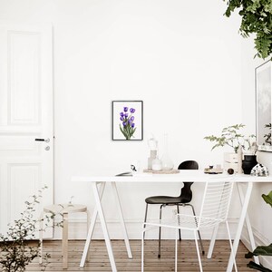 May include: A white table with a white chair and a black chair. A framed watercolor painting of purple tulips hangs on the wall above the table. There are plants in the room.