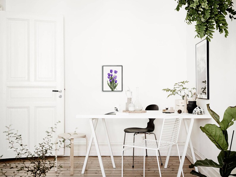 May include: A white table with a white chair and a black chair. A framed watercolor painting of purple tulips hangs on the wall above the table. There are plants in the room.