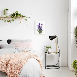 May include: A framed watercolor painting of a bouquet of purple tulips on a white background. The painting is hanging on a white wall in a bedroom setting.