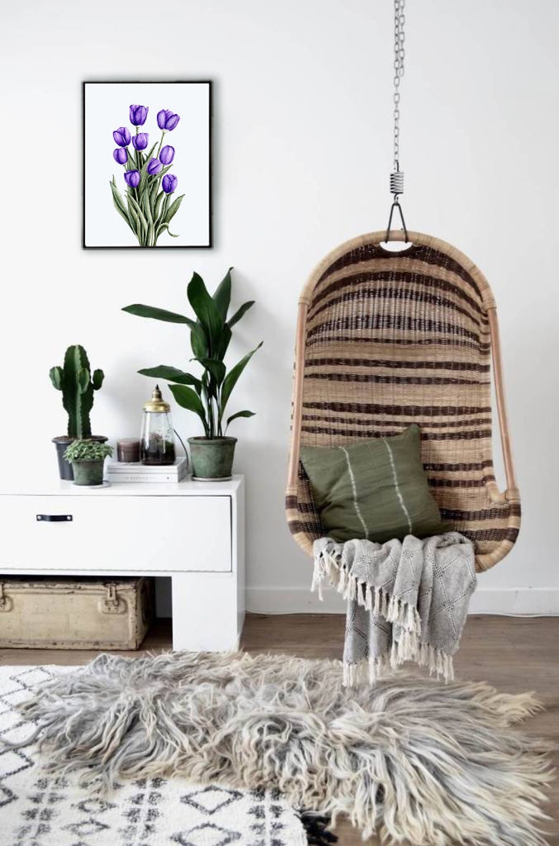 May include: A white wall with a framed print of purple tulips, a white dresser with a potted plant and a cactus, a hanging wicker chair with a green cushion and a white blanket, and a fluffy gray rug on the floor.