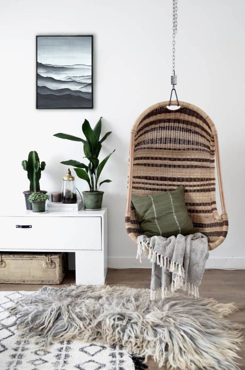 May include: A hanging wicker chair with a green cushion and a gray throw blanket. The chair is hanging from a white ceiling and there is a rug on the floor. There is a white cabinet with a cactus and a plant on top of it.