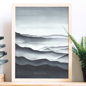 May include: A framed watercolor painting of a mountain range in shades of gray. The mountains are layered and appear to be covered in fog. The painting is set against a white background.