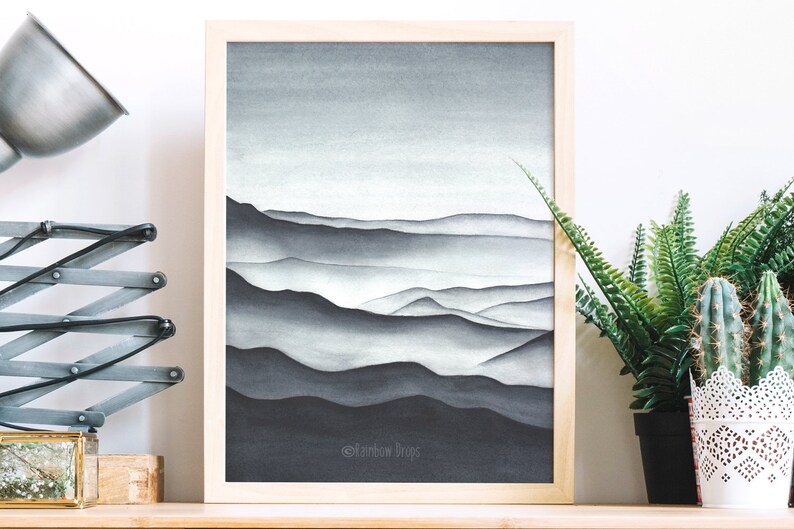 May include: A framed watercolor painting of a mountain range in shades of gray. The mountains are layered and appear to be covered in fog. The painting is set against a white background.