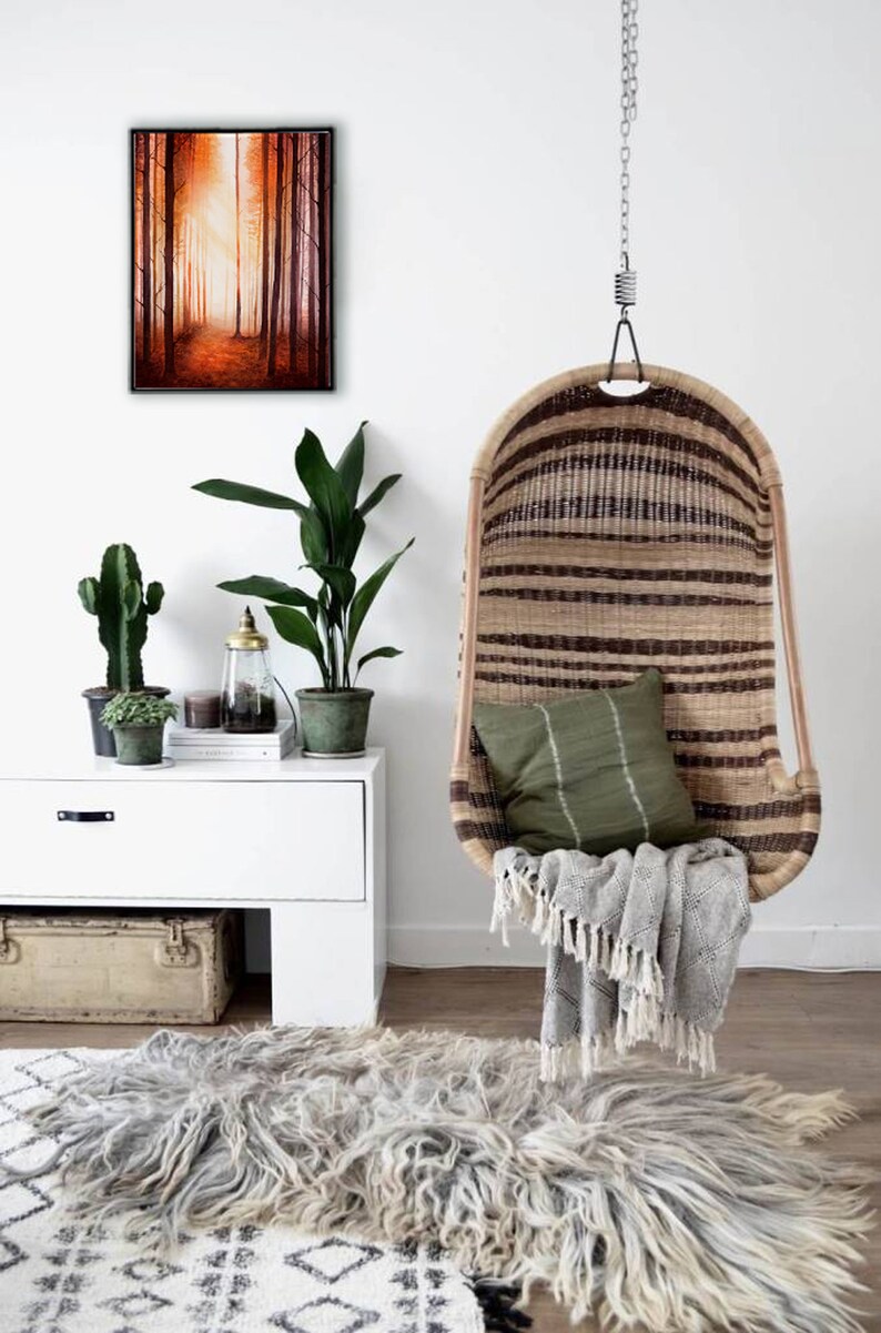May include: A hanging wicker chair with a green cushion and a grey throw blanket. The chair is hanging from a white ceiling with a chain. There is a rug on the floor and a white dresser with plants and a painting of a forest scene on the wall.