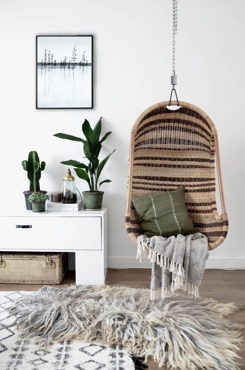 Pu&ograve; includere: Una sedia a dondolo in vimini con un cuscino verde e una coperta grigia. La sedia &egrave; appesa a un soffitto bianco con una catena. C'&egrave; una cassettiera bianca con un cactus e una pianta sopra. C'&egrave; un tappeto sul pavimento con un motivo bianco e nero.