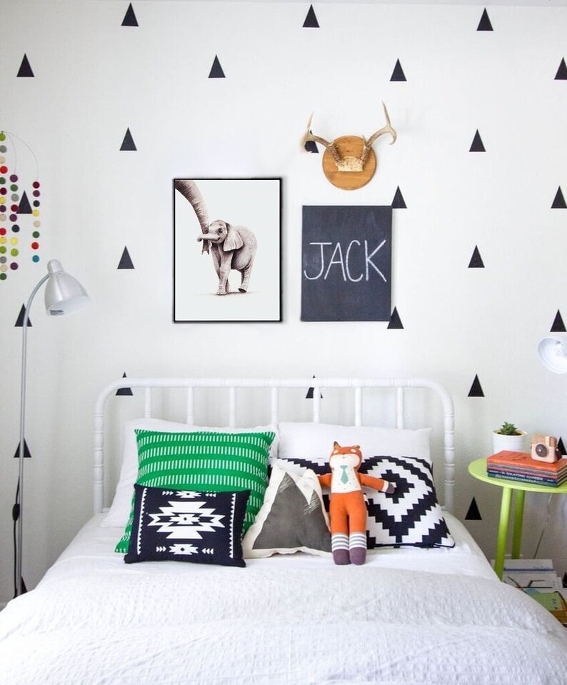 May include: A white bed with a green and white striped pillow, a black and white geometric pillow, a gray pillow with a mountain design, and a stuffed fox wearing a tie. The bed is in a room with white walls and black triangle decals. The name "JACK" is written on a black chalkboard hanging on the wall.