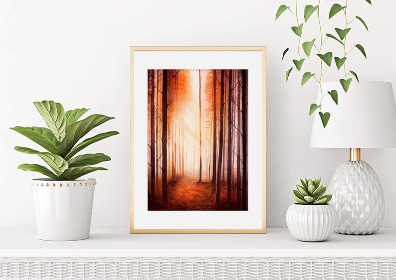 May include: A framed watercolour painting of a forest path with tall trees on either side. The trees are painted in shades of orange, red, and brown, and the path is lined with fallen leaves. The painting is set against a white wall with a potted plant and a lamp on either side.