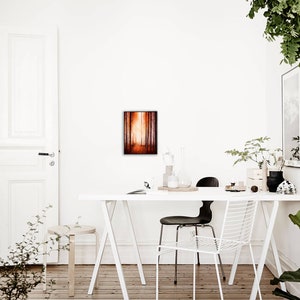 May include: A white table with a white chair and a black chair. A framed painting of a forest scene hangs on the wall behind the table. There are plants on the table and on the floor.