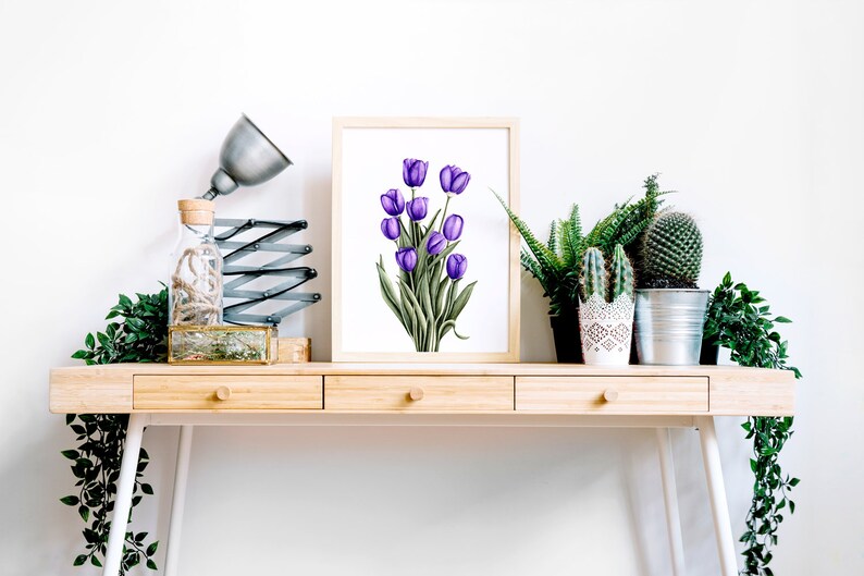 May include: A framed print of a watercolor painting of purple tulips on a white background. The print is displayed on a wooden desk with a lamp, a glass bottle, and potted plants.