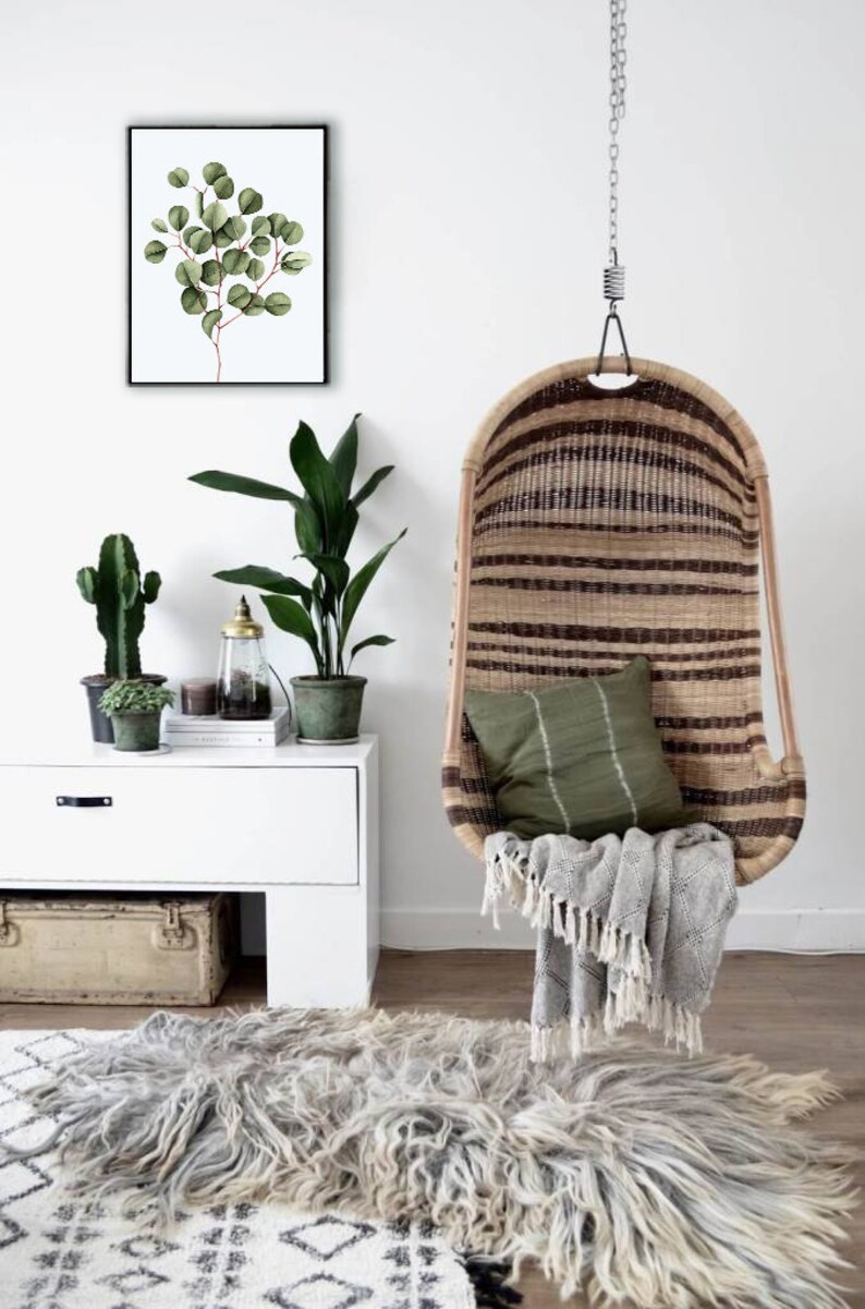 May include: A hanging wicker chair with a green cushion and a gray throw blanket. The chair is hanging from a white ceiling with a chain. There is a white dresser with a green plant and a cactus on top of it. There is a rug on the floor with a black and white pattern.