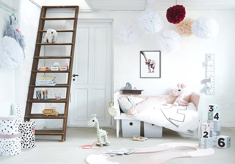 May include: A white and pink nursery with a wooden ladder shelf, a white crib with pink bedding, a stuffed elephant toy, and a wooden giraffe toy. The room is decorated with white pom-poms and a framed print of an elephant.