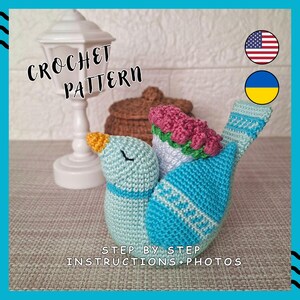 Könnte beinhalten: Ein gehäkeltes Vogelobjekt in Blautönen, mit gelbem Schnabel und rosa Blumendetail. Der Text "CROCHET PATTERN" und "STEP BY STEP INSTRUCTIONS+PHOTOS" sind sichtbar. Es handelt sich wahrscheinlich um ein Bastelprojekt.