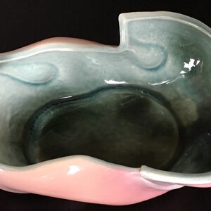 May include: A ceramic bowl with a unique, organic shape. The bowl is glazed in shades of pink, blue, and green.