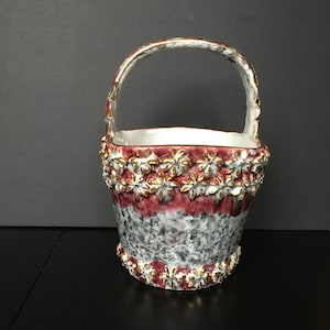May include: A white ceramic basket with a red and white speckled glaze. The basket has a gold trim and a handle. The basket is decorated with gold flowers.