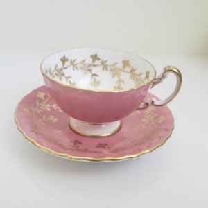 Peut inclure: Une tasse à thé et une soucoupe roses avec un motif floral doré. La tasse et la soucoupe sont toutes deux bordées d'une bande dorée.
