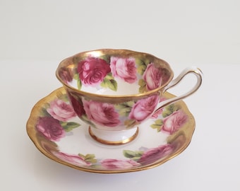 May include: A white teacup and saucer set with a pink and red rose floral pattern and gold trim.