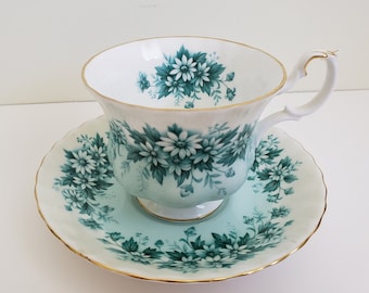 May include: A white teacup and saucer with a green floral pattern. The cup has a gold rim and the saucer has a scalloped edge.
