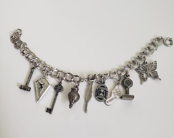 May include: A silver charm bracelet with a variety of charms, including a key, a butterfly, a feather, a heart, and a small hourglass. The charms are attached to a silver chain.