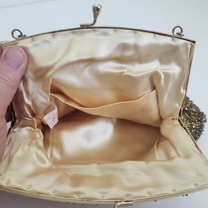 Pu&ograve; includere: Una borsa da sera in perline dorate con fodera in raso e una piccola tasca interna. La borsa ha una chiusura a scatto e una tracolla a catena.