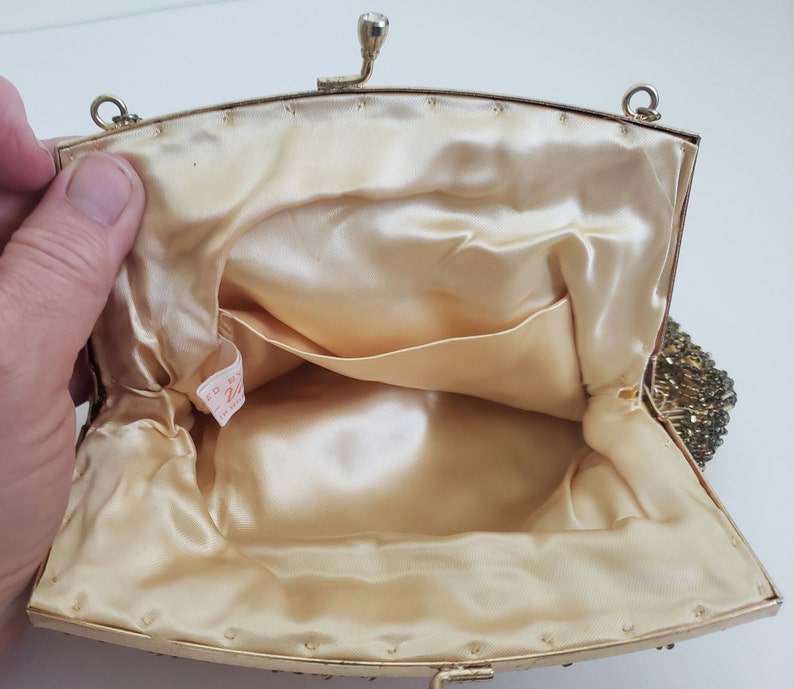 Pu&ograve; includere: Una borsa da sera in perline dorate con fodera in raso e una piccola tasca interna. La borsa ha una chiusura a scatto e una tracolla a catena.