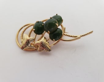 May include: A gold tone brooch with a cluster of four green cabochon stones set in a stylized floral design.