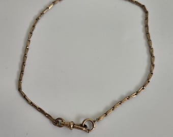 May include: A gold-toned metal chain necklace featuring a series of small, elongated, textured rectangular links connected in a continuous loop. The chain is secured with a circular spring ring clasp attached to a small swivel lobster claw hook.